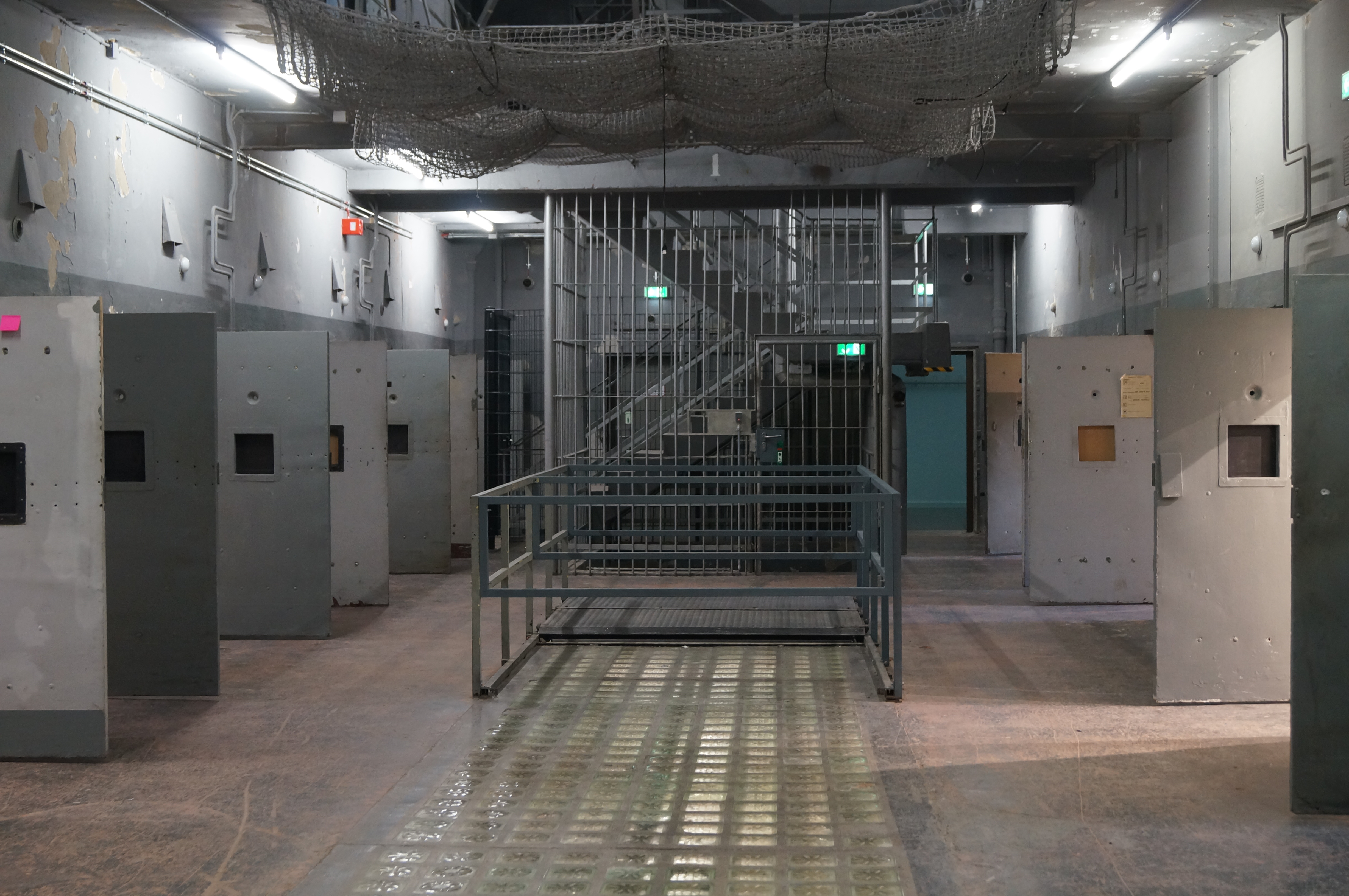 Das Foto zeigt eine Haftraumhalle in einem ehemaligen DDR Gefängnis, links und rechts sieht man offenen Türen. 