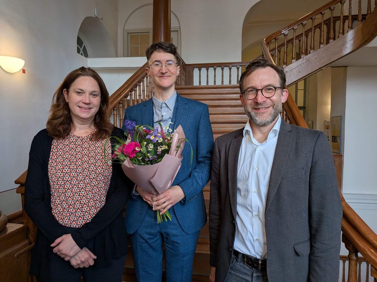 Agnes Bauer in der Fotomitte nach der erfolgreichen Verteidigung ihrer Dissertation mit Blumenstrauss und Prüfer*innen