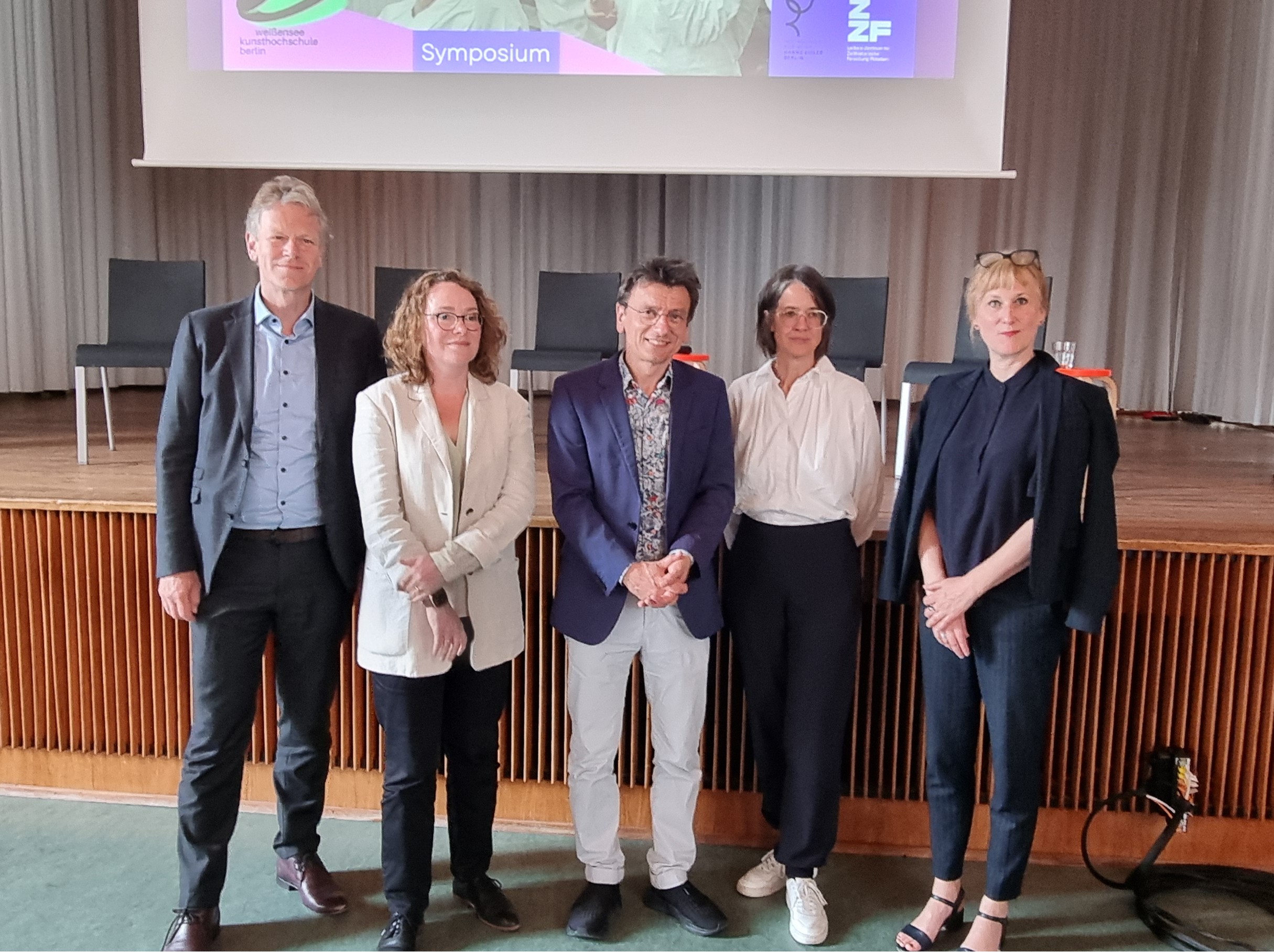 Das Foto zeitgt die fünf Teilnehmer *innes des 1. Panels des Symposiums "Kultur im Umbruch" - stehend vor der Bühne in der Aula der weißensee kunsthochschule berlin.