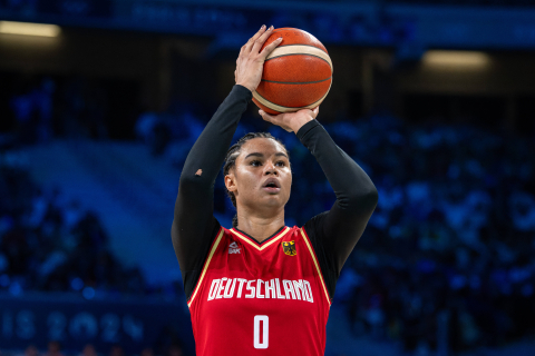 Das Foto zeigt eine Basketballspielerin, die zum Korbballwurf ansetzt und sehr konzentriert wirkt.