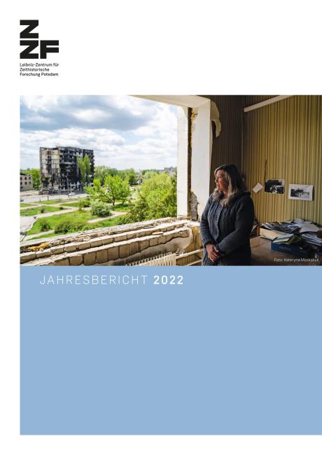 Cover des ZZF Jahresberichts 2022. Auf dem Titelbild ist das Foto einer Frau, die durch eine Fensteröffnung blickt, in der der Fensterrahmen und das Glas fehlen. Sie blickt auf ein ausgebranntes Hochhaus.