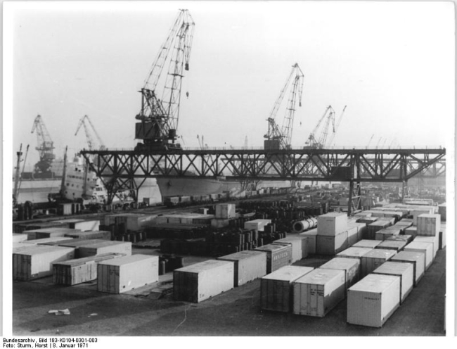 Das Bild zeigt den Überseehafen in Rostock. Zusehen sind im vorderen Teil des Bildes Container und im hinteren Teil des Bildes Kräne. Das Bild ist schwarz weiß.