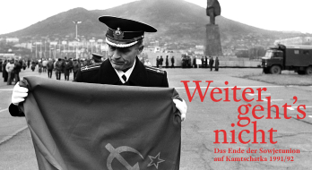 Das Bild zeigt einen Soldaten, der auf einem weitläufigen Platz eine Flagge zusammenfaltet.