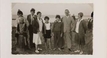 Familie Mann am Strand. Aufnahme vom 9. Februar 1930 in Nidden (heute Nida). Stehend, von links: Monika Mann mit einem Bauernmädchen, Golo Mann, Katia Mann, Michael Mann, Elisabeth Mann, Thomas Mann, Ilse Dernburg. Es fehlen Klaus und Erika. Fotograf: Fritz Krauskopf. Bildquelle: ETH-Bibliothek Zürich, Thomas-Mann-Archiv, TMA_AL30_6262