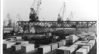 Das Bild zeigt den Überseehafen in Rostock. Zusehen sind im vorderen Teil des Bildes Container und im hinteren Teil des Bildes Kräne. Das Bild ist schwarz weiß.