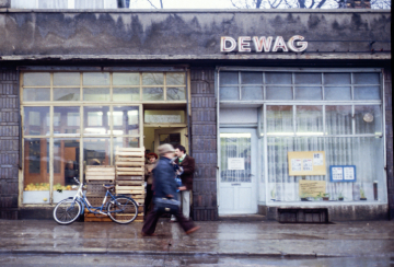 Bahnhofstraße in Merseburg, Lebensmittelgeschäft und DEWAG*-Filiale, Dezember 1980. Foto: Dietmar Rabich, via Wikimedia Commons, CC BY-SA 4.0. *Deutsche Werbe- und Anzeigengesellschaft, die DEWAG hatte das Werbemonopol in der DDR