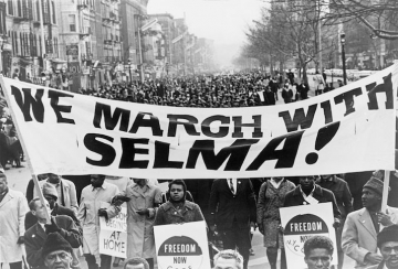 Originalbildunterschrift: Photograph shows marchers carrying banner "We march with Selma!" on street in Harlem, New York City, New York, 15 March 1965. Author: Stanley Wolfson, New York World Telegram & Sun. Quelle: Library of Congress's Prints and Photographs division, Digital-ID cph.3c35695, Lizenz: Public Domain.
