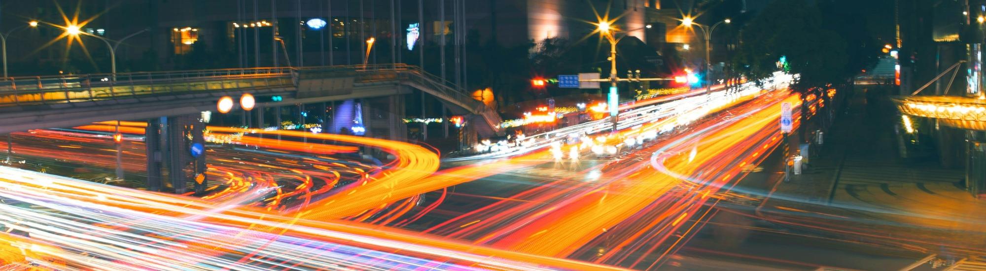 Aufnahme einer verkehrsreichen Kreuzung in Taipei bei Nacht, durch die lange Belichtungszeit hinterlassen die Lichter der Fahrzeuge rote und weiße Spuren.