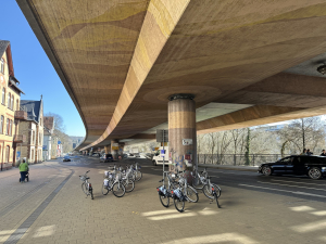 Berliner Stadtautobahn in unmittelbarer Nähe von Wohnhäusern. Unter der Trasse findet der Verkehr von Pkw, Fährrädern und Fußgänger*innen statt.