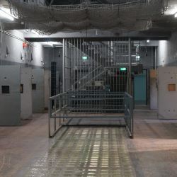Das Foto zeigt eine Haftraumhalle in einem ehemaligen DDR Gefängnis, links und rechts sieht man offenen Türen. 
